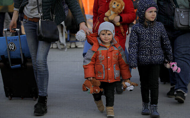 Un réfugié de guerre ukrainien marche aux côtés d'enfants tenant des jouets après avoir traversé la frontière en ferry au poste frontalier Isaccea-Orlivka en Roumanie, le jeudi 24 mars 2022. (Crédit : AP Photo/Andreea Alexandru)
