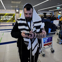 Un Juif ukrainien qui a fui l'Ukraine prie couvert d'un châle de prière à l'aéroport international de Chisinau en Moldavie, alors qu'il se rend en Israël, le 6 mars 2022. (Crédit : Nati Shohat/Flash90)