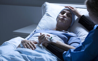Un bénévole au chevet d'une femme mourant d'une tumeur dans une chambre d'hôpital. (Crédit : iStock)