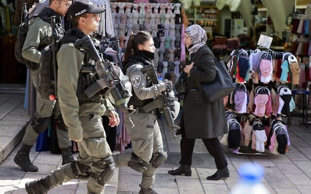 Une Palestinienne passe devant les forces de sécurité israéliennes patrouillant dans la vieille ville de Jérusalem le 31 mars 2022. (Crédit : Photo de Menahem Kahana/AFP)