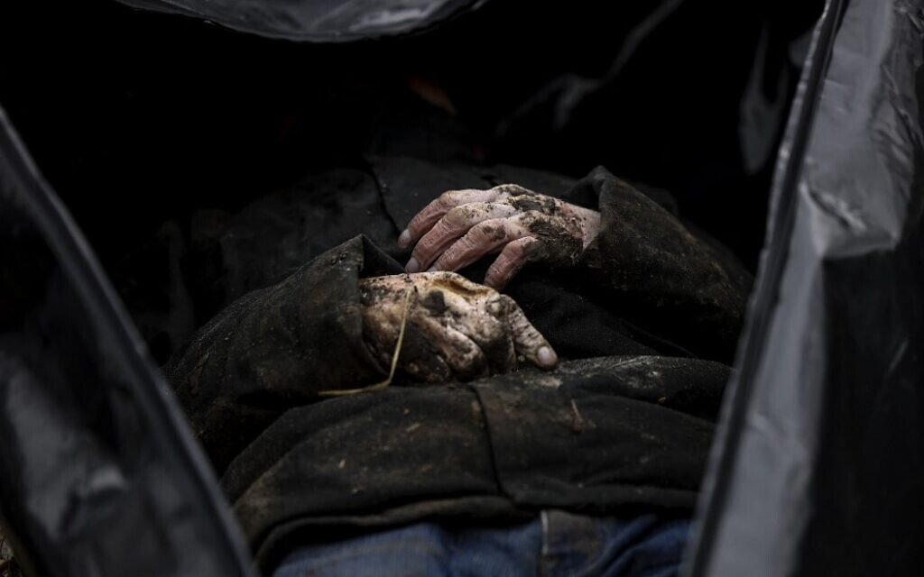 Un corps est partiellement photographié alors que des sacs mortuaires sont rassemblés dans un cimetière de Boutcha, au nord de Kiev, pour identification, après que des centaines de civils ont été retrouvés morts dans les zones d'où les troupes russes se sont retirées autour de la capitale ukrainienne, le 6 avril 2022.(Crédit: Ronaldo Schemidt / AFP).