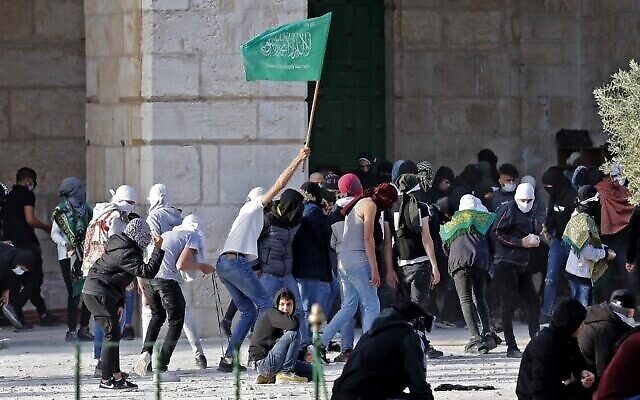 Des Palestiniens - l'un d'entre eux brandit un drapeau du Hamas - affrontent la police israélienne à la mosquée al-Aqsa, sur le mont du Temple de Jérusalem, le 22 avril 2022. (Crédit : Ahmad Gharabli/AFP)