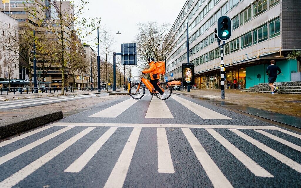 Un cycliste travaillant pour une société de livraison roule sur une route vide dans le centre-ville de Rotterdam, le 19 décembre 2021, au premier jour de confinement aux Pays-Bas pendant la période de Noël pour tenter d'arrêter une vague de la variante Omicron du coronavirus. (Crédit : Marco de Swart/ANP/AFP