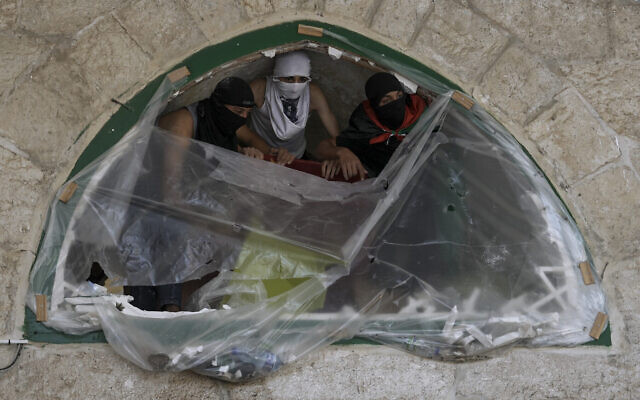 Des Palestiniens masqués prennent position lors d'affrontements avec les forces de sécurité israéliennes sur le mont du Temple dans la Vieille Ville de Jérusalem, le 15 avril 2022. (Crédit : Mahmoud Illean/AP)