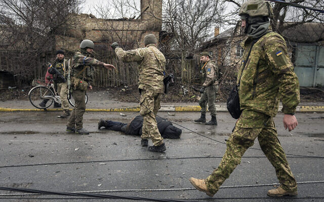 Des militaires ukrainiens autour de la dépouille d'un civil dans une rue de Boutcha, dans la banlieue de Kyiv, le 2 avril 2022. (Crédit : AP Photo/Vadim Ghirda)