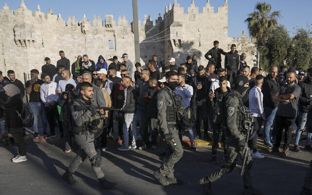 Des Palestiniens regardent les forces de sécurité israéliennes patrouiller près de la porte de Damas, juste à l'extérieur de la vieille ville de Jérusalem, le 20 avril 2022. (Crédit: AP/Mahmoud Illean)