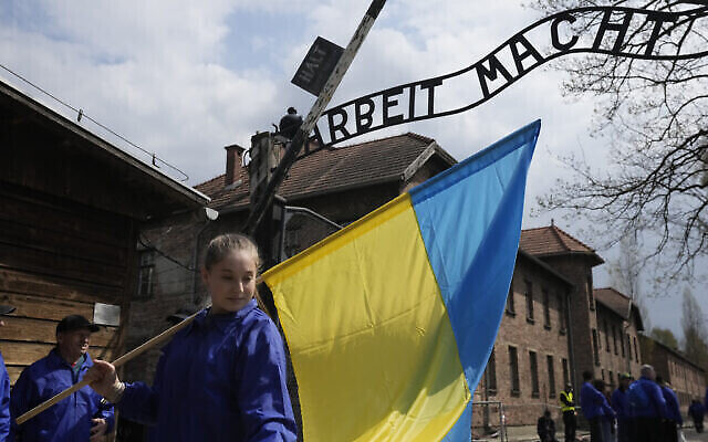 Une femme tient un drapeau ukrainien au camp de concentration nazi d'Auschwitz à Oswiecim, en Pologne, le 28 avril 2022. (Crédit : AP Photo/Czarek Sokolowski)