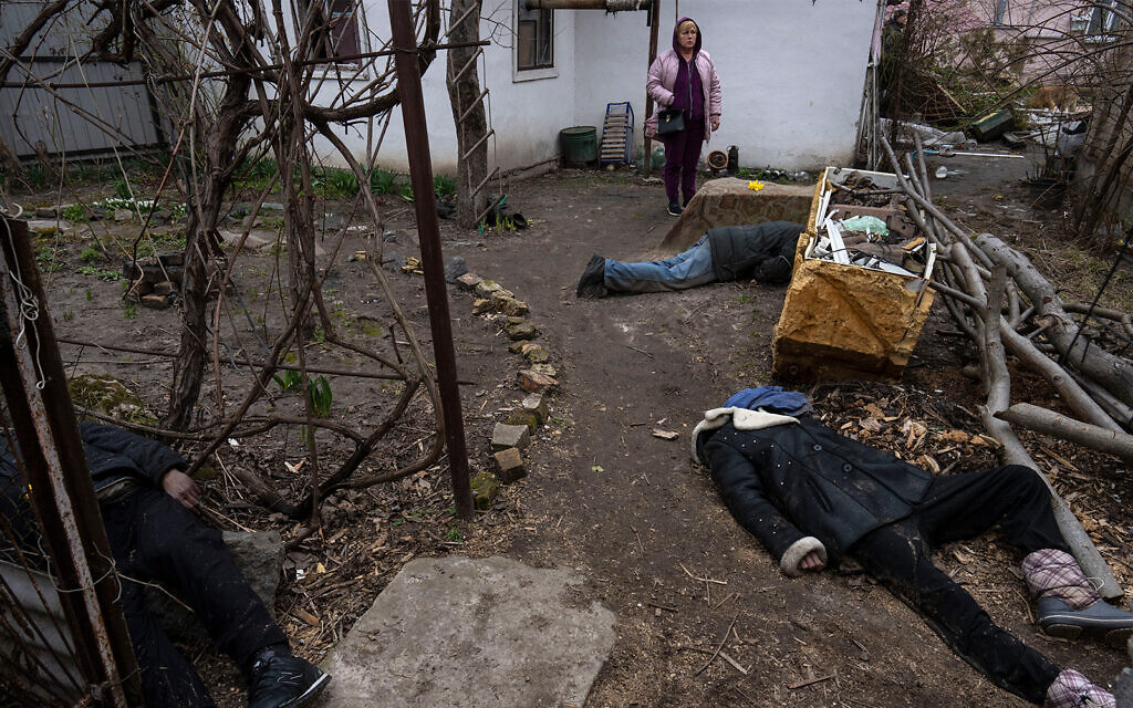 Une femme se tient à côté de trois corps dans la cour d'une maison à Bucha, dans la banlieue de Kiev, en Ukraine, le 5 avril 2022. (Crédit : AP Photo/Rodrigo Abd)