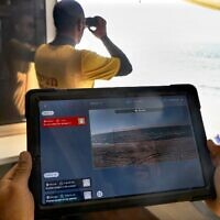 Un maître-nageur porte une tablette, affichant un programme appelé SIghtbit, tandis qu'un autre surveille l'horizon sur une plage de la ville côtière méditerranéenne d'Ashdod, le 14 février 2022, alors qu'ils font la démonstration du programme d'intelligence artificielle visant à détecter les menaces de noyade. (Crédit : MENAHEM KAHANA / AFP))