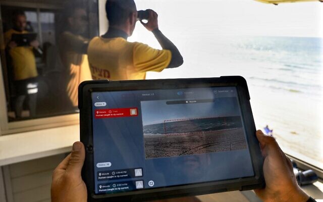 Un maître-nageur porte une tablette, affichant un programme appelé SIghtbit, tandis qu'un autre surveille l'horizon sur une plage de la ville côtière méditerranéenne d'Ashdod, le 14 février 2022, alors qu'ils font la démonstration du programme d'intelligence artificielle visant à détecter les menaces de noyade. (Crédit : MENAHEM KAHANA / AFP))