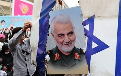 Des Iraniens se préparent à incendier un drapeau israélien près d'une photographie de feu le général iranien Qasem Soleimani pendant un rassemblement organisé pour la journée al-Quds à Téhéran, le 29 avril 2022. (Crédit : AFP)