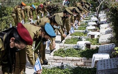 Le 13 avril 2021, au cimetière militaire de Kiryat Shaul, dans la ville côtière méditerranéenne de Tel-Aviv, des soldats placent des drapeaux israéliens arborant des ceintures noires au-dessus du mot hébreu « Souvenir » sur des tombes, en hommage aux soldats tombés le jour du Yom HaZikaron. (Crédit : Jack Guez/AFP)