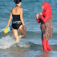 Illustration : Des femmes, dont l'une porte un "burkini", un maillot de bain intégral conçu pour les femmes musulmanes, marchent dans l'eau sur la plage de Ghar El Melh près de Bizerte, au nord-est de la capitale Tunis, le 16 août 2016. (Crédit : AFP/FETHI BELAID)