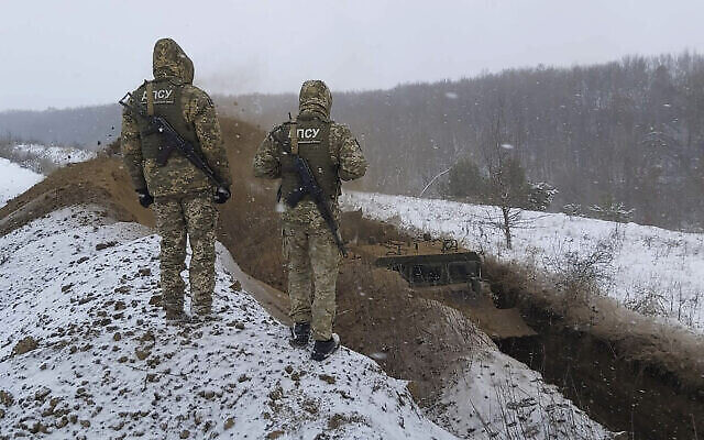 Des gardes-frontières ukrainiens observent un véhicule spécial qui creuse une tranchée à la frontière entre l'Ukraine et la Russie près de Sumy, en Ukraine, le 21 décembre 2021. (Crédit : Bureau de presse des gardes-frontières ukrainiens/AP)