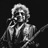 Le chanteur américain Bob Dylan souriant lors de son spectacle au stade olympique de Colombes, en France, le 24 juin 1981. (Crédit: AP Photo/Herve Merliac, File)