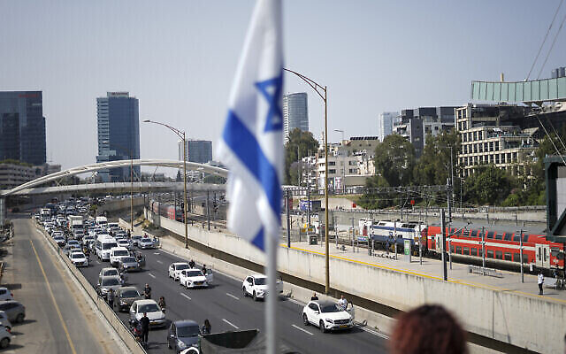 Des Israéliens se tiennent immobiles à côté de leur voiture sur une autoroute alors que retentit pendant deux minutes la sirène en mémoire des victimes de la Shoah à Tel-Aviv, en Israël, le 28 avril 2022 (Crédit : AP Photo/Ariel Schalit)