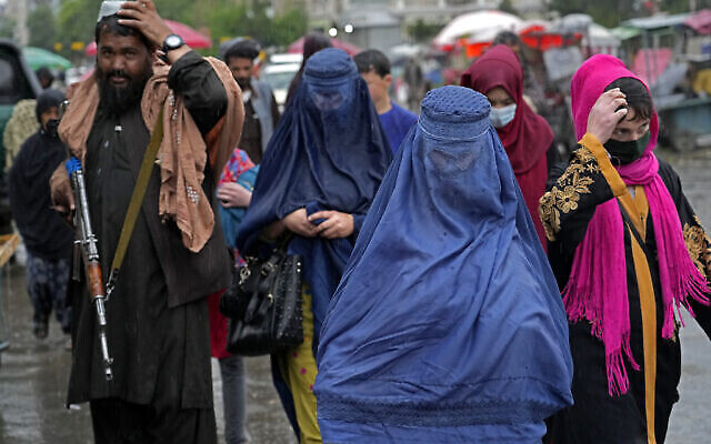 Des femmes afghanes marchent dans le vieux marché alors qu’un combattant taliban monte la garde, au centre-ville de Kaboul, en Afghanistan, le mardi 3 mai 2022. Le samedi 7 mai, les dirigeants talibans de l’Afghanistan ont ordonné à toutes les Afghanes de porter des vêtements de la tête aux pieds en public (Crédit : AP Photo/Ebrahim Noroozi).