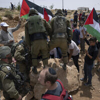 Des soldats israéliens empêchent des militants pacifistes palestiniens, israéliens et étrangers de déplacer un rocher qui bloque une route passant près de l’implantation de Mezbi yair, à Masafer Yatta, en Cisjordanie, le 13 mai 2022. (Crédit: AP/Nasser Nasser)
