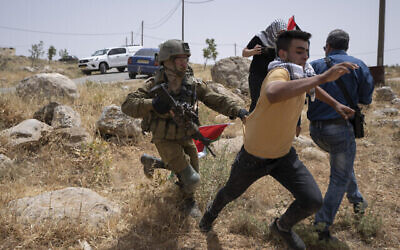 Un soldat israélien poursuit un manifestant alors que des militants pacifistes palestiniens, israéliens et étrangers tentent d'ouvrir une route qui passe près de l'avant-poste israélien de Mitzpe Yair à Masafer Yatta en Cisjordanie, le 13 mai 2022. (Crédit: AP Photo/Nasser Nasser)
