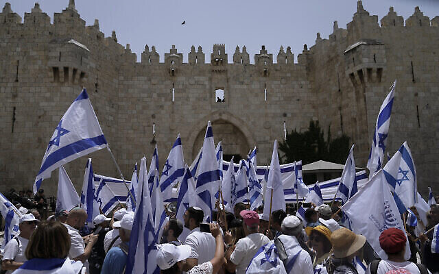 Des Israéliens brandissent des drapeaux devant la porte de Damas, à l’extérieur de la Vieille Ville de Jérusalem pour célébrer Yom Yeroushalayim, le 29 mai 2022 (Crédit : AP Photo/Mahmoud Illean)