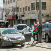 Un Israélien retire un drapeau palestinien d’un lampadaire dans la ville de Hawara, en Cisjordanie, près de Naplouse, le 22 mai 2022 (Crédit : Nasser Ishtayeh/Flash90)