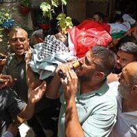Des endeuillés portent le corps d’Ali Harb, qui aurait été poignardé à mort par un résident d'implantation israélien, lors de ses funérailles dans le village d’Iskaka, au nord de la Cisjordanie, le 22 juin 2022. (Crédit : Jaafar Ashtiyeh/AFP)