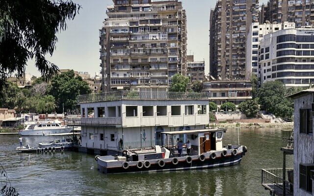 L'un des maisons flottantes habituellement amarrés sur l'une des rives du Nil entre le quartier de Zamalek, au Caire, la capitale égyptienne (à droite), et le quartier d'Agouza, dans la ville jumelle de Gizeh (à gauche), est remorqué par les autorités le 27 juin 2022, dans le cadre d'un décret plus large visant à nettoyer toutes les rives du fleuve dans la région. (Crédit : Khaled DESOUKI / AFP)
