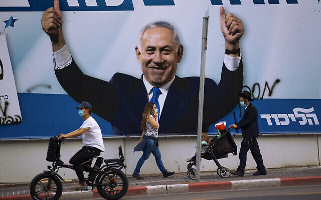 Passants devant un panneau d’affichage électoral pour le parti Likud, donnant à voir un portrait de son chef, Benjamin Netanyahu, à Ramat Gan, Israël, 21 mars 2021. (Crédit : AP Photo/Oded Balilty)