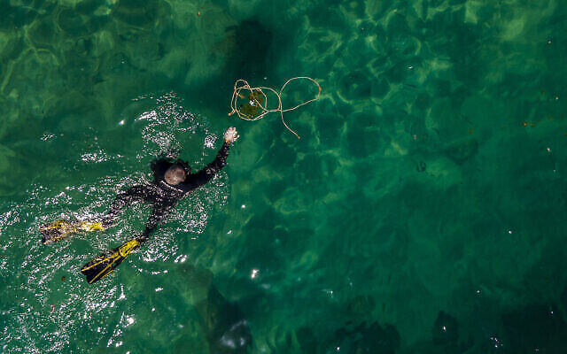 Un plongeur bénévole ramasse des déchets, à l'occasion de la Journée mondiale des océans, dans le port romain de l’ancienne Méditerranée de Césarée, en Israël, le 10 juin 2022. (Crédit : AP Photo/Ariel Schalit)