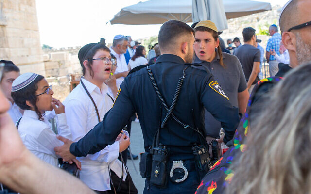 Un officier de police se tient entre un groupe de jeunes ultra-orthodoxes et une cérémonie de bar-mitsva dans la section égalitaire du Mur Occidental, le 30 juin 2022. (Crédit: Laura Ben-David)