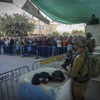 Des soldats israéliens montent la garde alors que des Palestiniens passent un poste de contrôle pour assister à la prière du vendredi à la mosquée Al-Aqsa de Jérusalem, près de la ville de Bethléem en Cisjordanie, le 29 avril 2022. (Crédit: Wisam Hashlamoun/ Flash90/ Dossier)