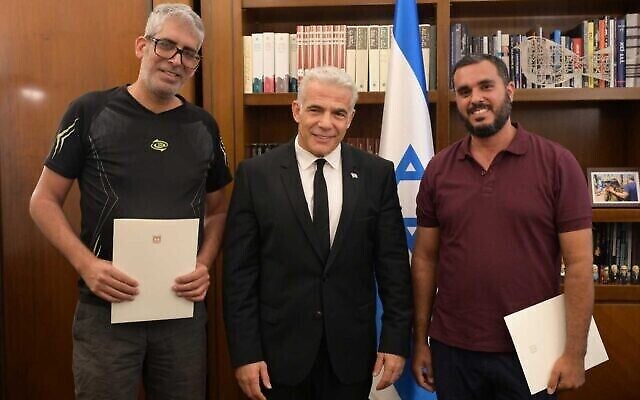 Le Premier ministre Yair Lapid, au centre, félicite Meshi Ben Ami, à gauche, et Haim Naim, au cabinet du Premier ministre, à Jérusalem, le 20 juillet 2022. (Crédit : Amos Ben Gershom/GPO)