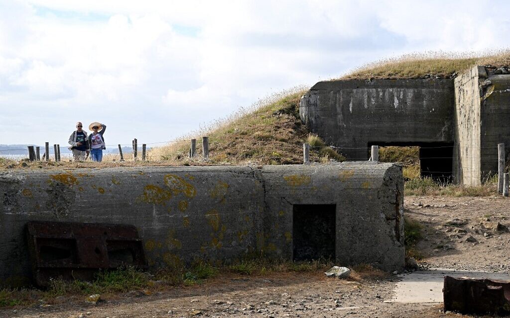 Des touristes passent devant des bunkers et des épaves de canons d'artillerie sur l'île de Cézembre, au large de Saint-Malo, le 4 août 2022. (Crédit : Damien MEYER / AFP)
