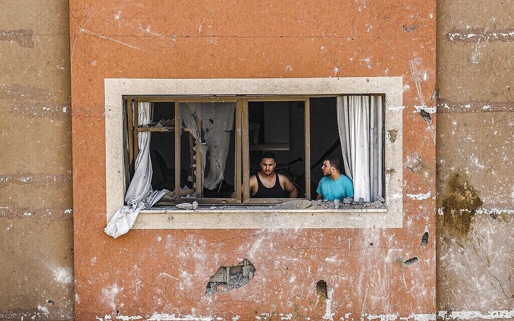 Des hommes regardent par une fenêtre brisée à la suite d'une frappe aérienne israélienne dans la ville de Gaza, le 6 août 2022. (Crédit : Mahmoud Hams/AFP)