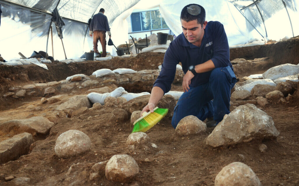 Kfir Arbiv, directeur des fouilles de l'Autorité des antiquités d'Israël, nettoie une pierre de baliste vieille de 2000 ans sur le site de fouilles du Russian Compound à Jérusalem. (Crédit : Yoli Schwartz/Autorité des antiquités d’Israël)