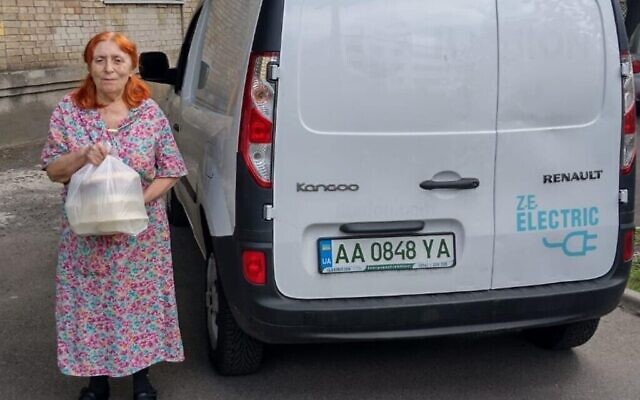 Femme tenant un colis d'aide humanitaire livré par une voiture électrique appartenant aux Fédérations juives d’Ukraine à Kiev, en Ukraine, le 1er août 2022. (Avec l’aimable autorisation des Fédérations juives d’Ukraine / via la JTA)