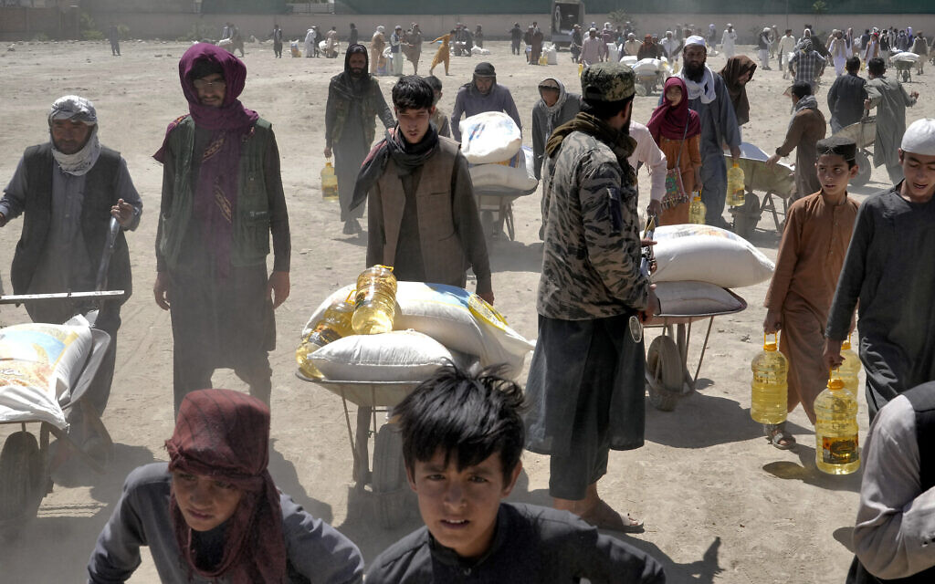 Un combattant taliban montant la garde alors que des personnes reçoivent des rations alimentaires distribuées par un groupe d'aide humanitaire chinois, à Kaboul, en Afghanistan, le 30 avril 2022. (Crédit : Ebrahim Noroozi/AP)