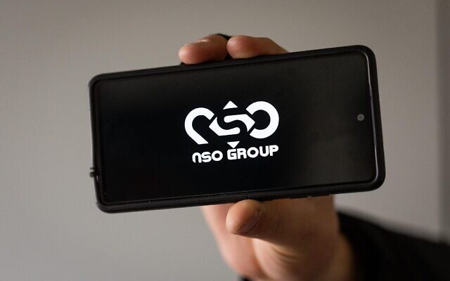 Illustration : Un homme tenant un téléphone avec le logo du groupe NSO. (Crédit : Yonatan Sindel/Flash90)