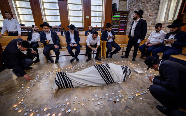 Des hommes prient à côté de la dépouille du rabbin Shalom Cohen, chef spirituel du parti ultra-orthodoxe Shas, dans une synagogue de Jérusalem, le 22 août 2022. (Crédit :  Yonatan Sindel/Flash90)