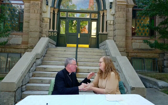 Rebecca Stanfel, présidente du conseil d'administration du Montana Jewish Project, serrant la main de l'évêque Austin Vetter du diocèse d'Helena lors de la cérémonie de restitution du bâtiment à la communauté juive. (Crédit : Capture d'écran/Facebook Live, via JTA)
