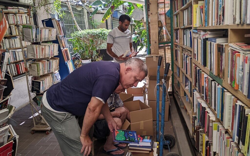  Les quatre enfants de Yosef Halper ont tous travaillé dans la librairie à différents moments, mais son fils, qui est professeur d'éducation physique, aide toujours pendant les étés. Halper et son fils regardant des boîtes de livres achetés, le 6 juillet 2022 à Tel Aviv. (Crédit : Melanie Lidman/Times of Israel)