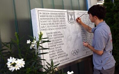 Un homme repeint l'inscription d'une plaque commémorative devant un immeuble d'habitation de la Conollystrasse 31 dans l'ancien village olympique de Munich, dans le sud de l'Allemagne, le 17 août 2022, où les membres de l'équipe olympique israélienne étaient logés pendant les Jeux olympiques de Munich de 1972. (Crédit : INA FASSBENDER / AFP)