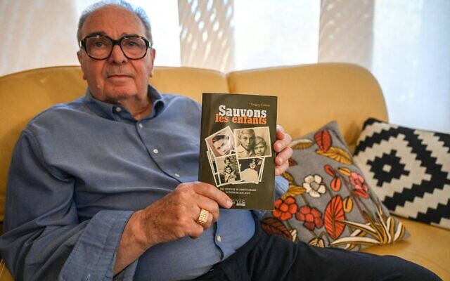 Eric Adamski, 84 ans, survivant du sauvetage d'enfants à la gare de Lille le 11 septembre 1942, alors qu'il avait 4 ans, chez lui, à Lille, dans le nord de la France, tenant un livre relatant l'histoire de ce sauvetage, le 6 septembre 2022. (Crédit : DENIS CHARLET / AFP)