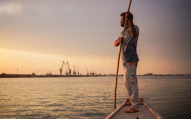 Le pêcheur irakien Naim Haddad, 40 ans, se tient pieds nus sur son bateau au coucher du soleil sur Chatt al-Arab, le confluent des fleuves du Tigre et de  l'Euphrate qui se jette dans le Golfe, près de la ville de Bassora dans le sud de l'Irak, le 12 février 2022. (Crédit : Ayman HENNA / AFP)