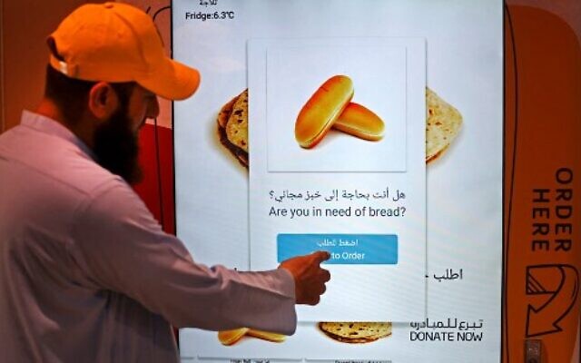 Un homme commandant des articles dans un distributeur automatique qui distribue du pain gratuit, à Dubaï, le 22 septembre 2022. (Crédit : Karim Sahib/AFP)