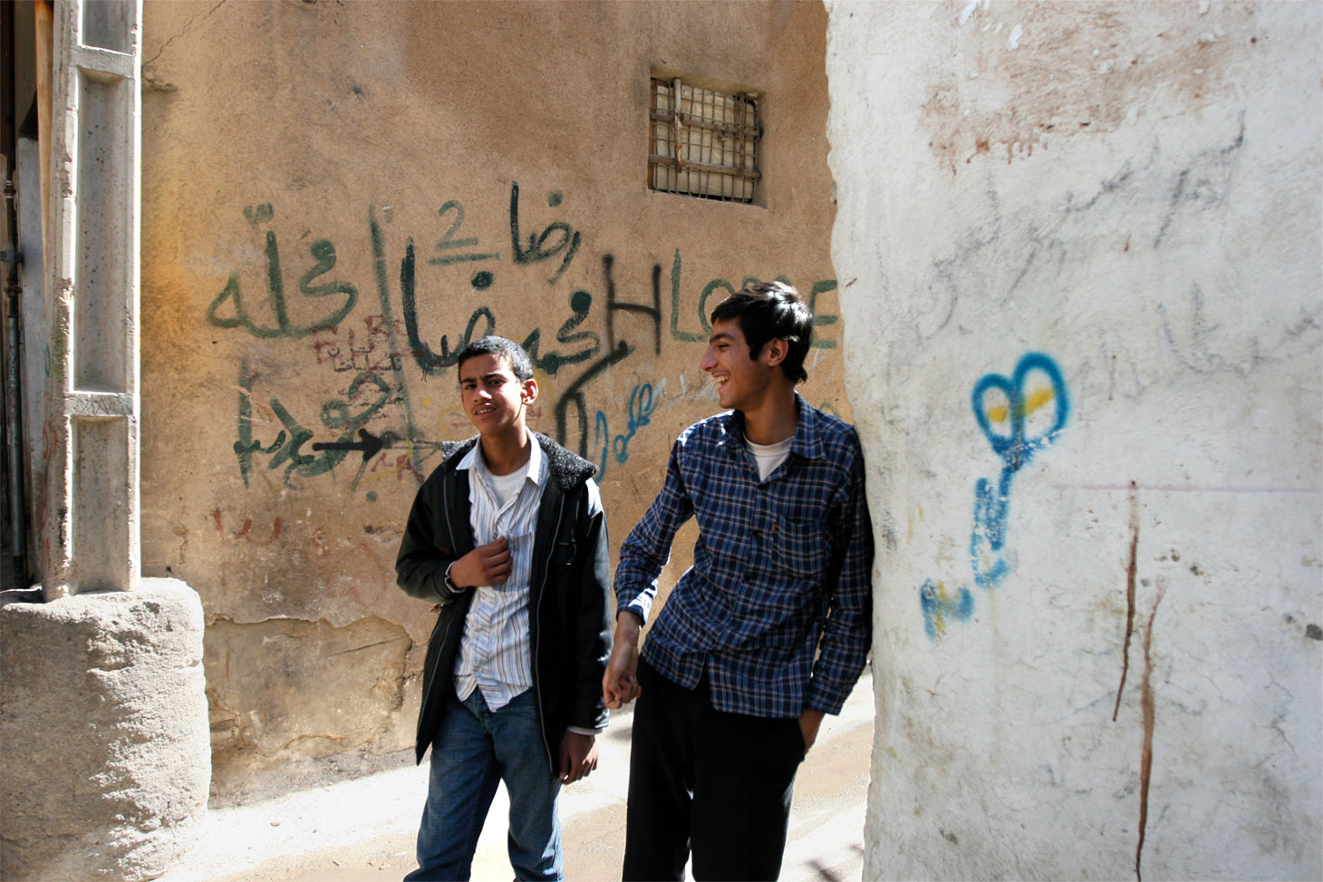 Deux jeunes hommes marchent dans un quartier juif de Shiraz. Sur le mur derrière eux, un terme péjoratif pour les Juifs est écrit en graffiti. (Crédit : Hassan Sarbakhsian/via JTA)