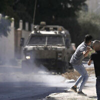 Un Palestinien lançant des pierres sur un véhicule militaire israélien après une opération militaire dans la ville de Jénine, en Cisjordanie, le 28 septembre 2022. (Crédit : Majdi Mohammed/AP)