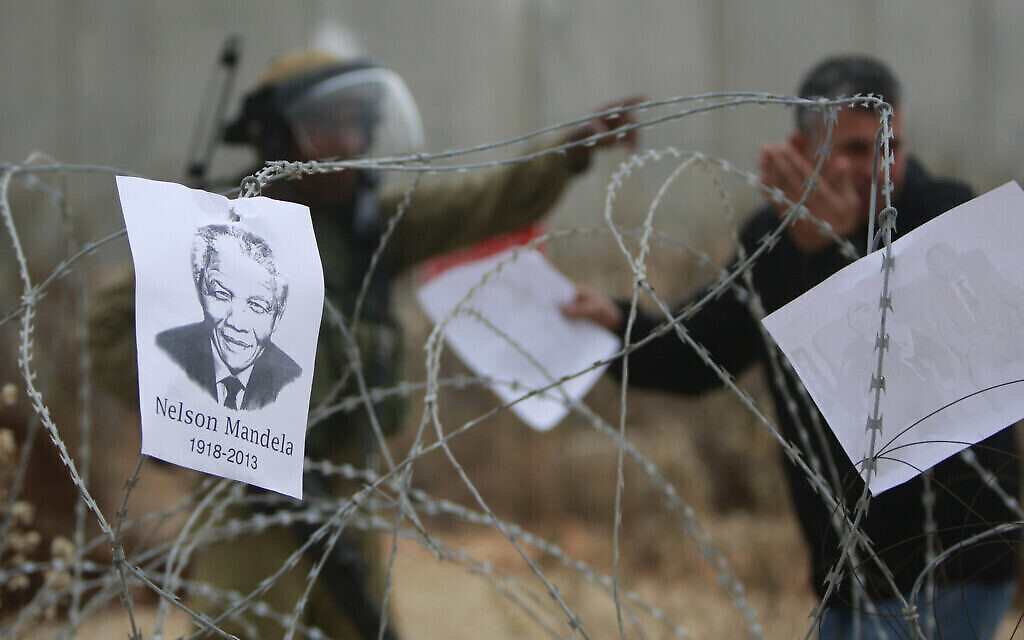 Un portrait du défunt dirigeant sud-africain Nelson Mandela est accroché à une clôture tandis qu’un soldat israélien parle avec un Palestinien venu pour une manifestation hebdomadaire contre la barrière de séparation, dans le village de Bilin en Cisjordanie, près de Ramallah, le 6 décembre 2013. (Crédit : AP Photo/Majdi Mohammed)