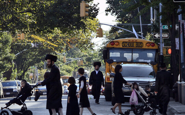 Illustration : Des enfants et des adultes traversant la rue devant un bus scolaire à Borough Park, dans le quartier de Brooklyn qui abrite de nombreuses familles juives ultra-orthodoxes, à New York, le 20 septembre 2013. (Crédit : AP Photo/Bebeto Matthews)