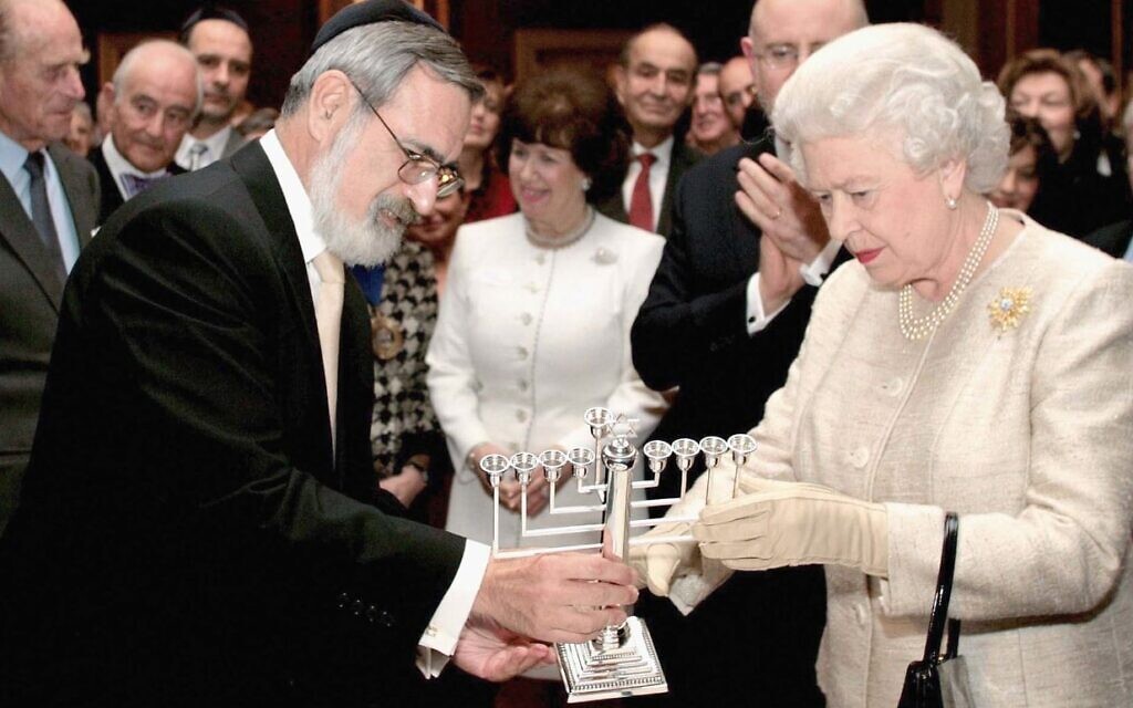 Le grand rabbin britannique Jonathan Sacks, aujourd'hui décédé, offrant à la reine une ménorah lors d'une réception au palais de Saint-James pour marquer le 350e anniversaire du rétablissement de la communauté juive en Grande-Bretagne, à Londres, le 28 novembre 2006. (Crédit : Tim Graham Picture Library/Getty Images via JTA)